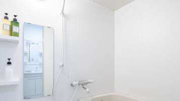 A modern bathroom with a white bathtub, a handheld showerhead, and a mirror.