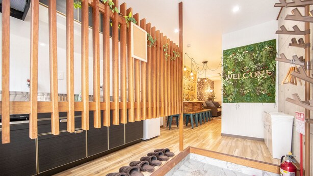 A modern reception area with a wooden reception desk, a welcome sign, and a fire extinguisher. - Bar Hostel Shikanzima (Osaka)