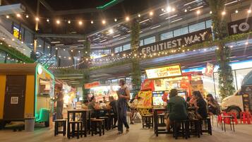 An outdoor dining area with tables and chairs, a sign reading "FRUITIEST WAY", and a food truck in the background.