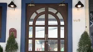 Une porte en bois à deux battants, dotée de panneaux de verre, flanquée de deux lampes fixées au mur, et un panneau indiquant le numéro « 44/8 » au-dessus.