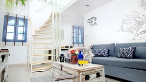Un salon moderne avec un canapé gris, des coussins à motifs, une table basse en bois et un escalier avec des rampes blanches.
