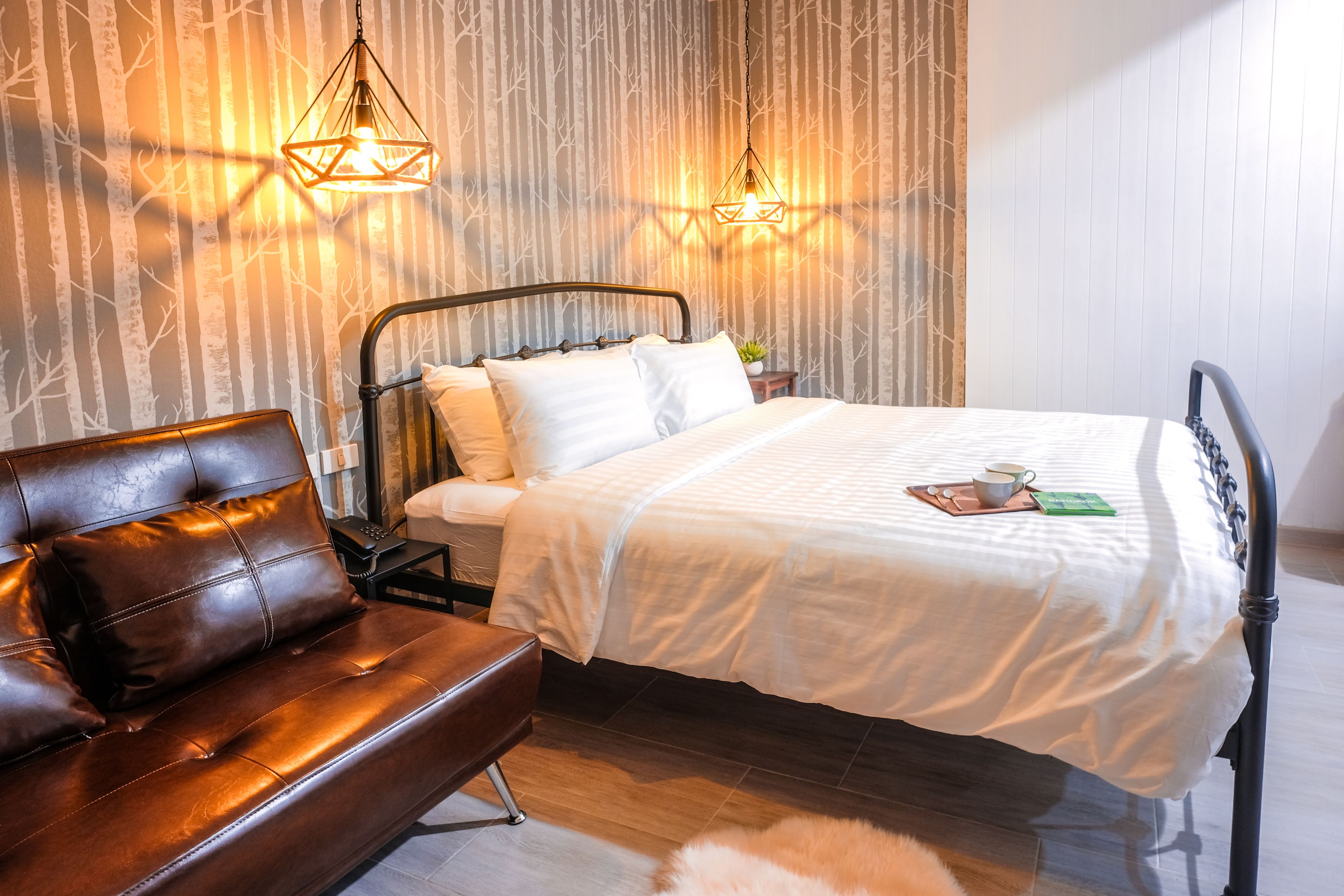 A bedroom with a bed, a brown leather sofa, and two wall-mounted lamps.