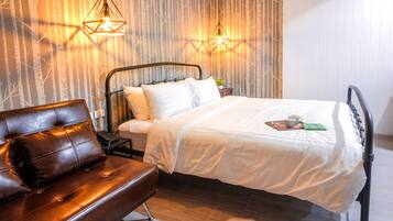 A bedroom with a bed, a brown leather sofa, and two wall-mounted lamps.