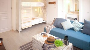 Une chambre avec un lit superposé, un canapé bleu orné de coussins à motifs, une table de chevet avec un chapeau et une plante, et une commode avec un miroir.