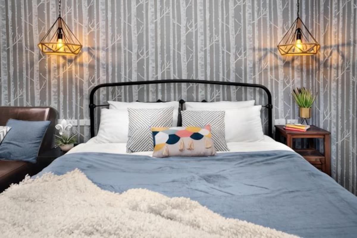 A bed with a black metal frame, white and patterned pillows, a fluffy white blanket, and two bedside tables with lamps.