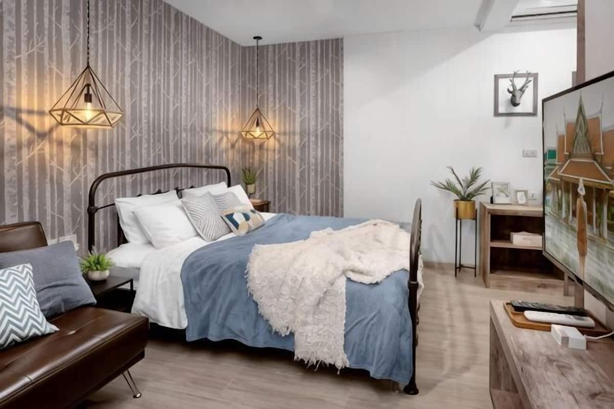 Ein modernes Schlafzimmer mit Bett, Nachttischen, Schreibtisch, Fernseher und Wanduhr.