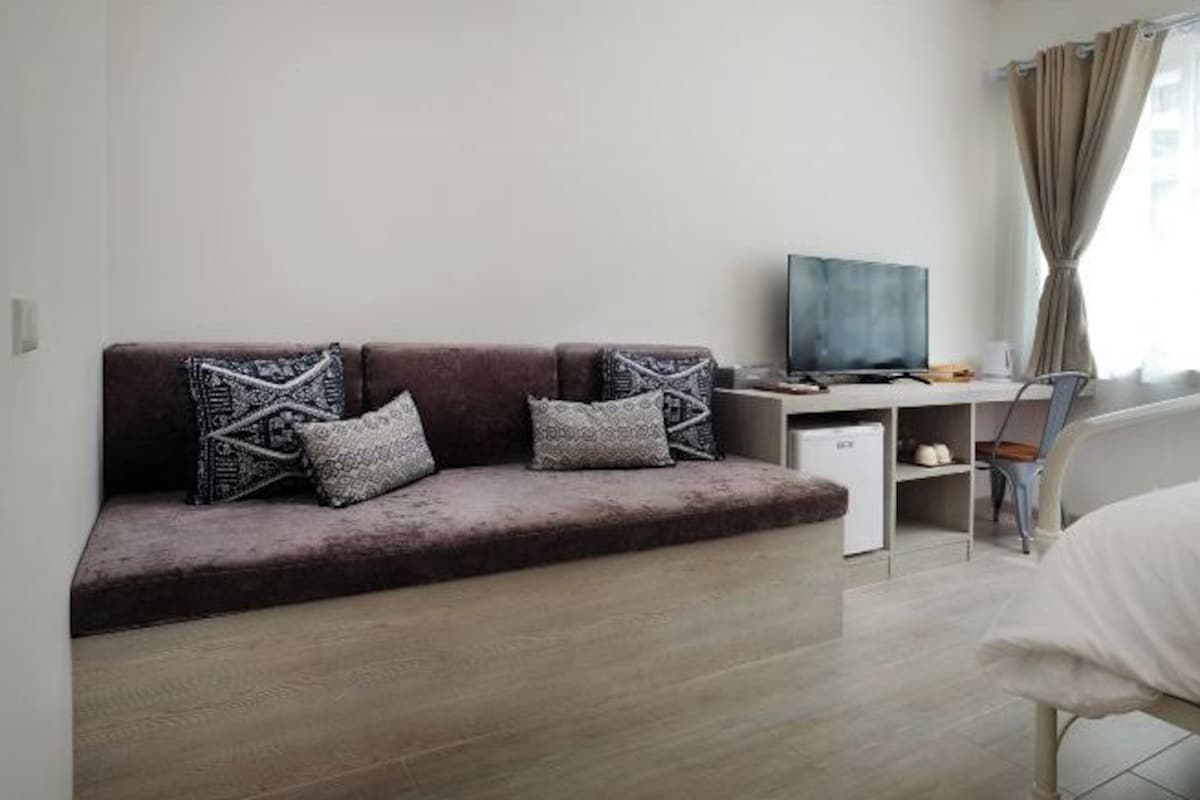 A modern hotel room with a brown sofa, a flat-screen TV, a small desk, and a chair.