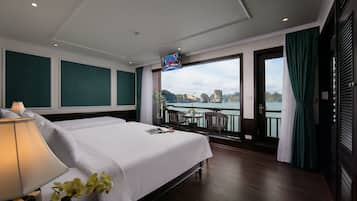 A hotel room with a large bed, a TV mounted on the wall, a view of a body of water, and a balcony with outdoor seating.