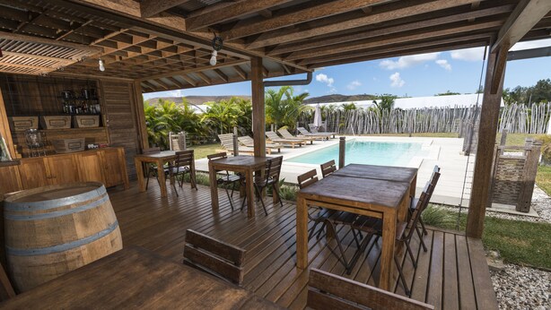 Una terraza de madera con mobiliario exterior, una piscina y una zona de bar.