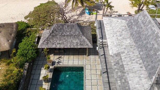 Une propriété située en bord de mer, dotée d’une piscine, d’une structure à toit de chaume et offrant une vue sur l’océan.