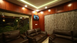 A modern living room with leather sofas, a flat-screen TV mounted on the wall, and a large window with a view of greenery. - Mrk Inn (Puducherry)