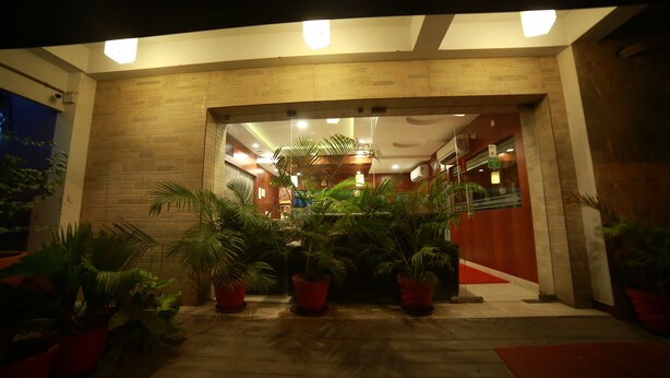 A building entrance with a brick facade, potted plants, and a red carpet leading to the entrance. - Mrk Inn (Puducherry)