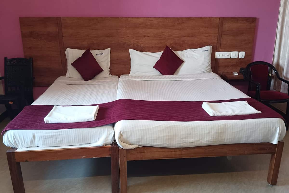 A double bed with a wooden headboard, two pillows, a white blanket, and a red throw.