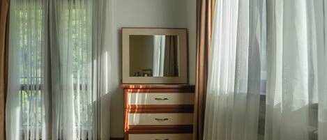 Una habitación con un aparador de madera, un espejo y cortinas de encaje.