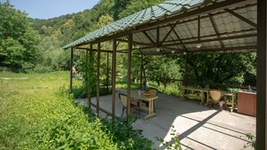 A covered outdoor patio with a table and chairs, surrounded by greenery and a mountainous backdrop. - Ariana Family Hotel (Dilijan)