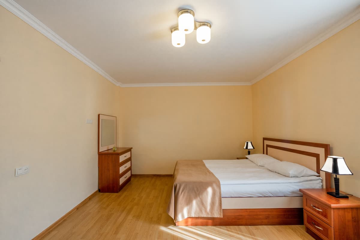 A bedroom with a bed, bedside table, dresser, and a ceiling light fixture.