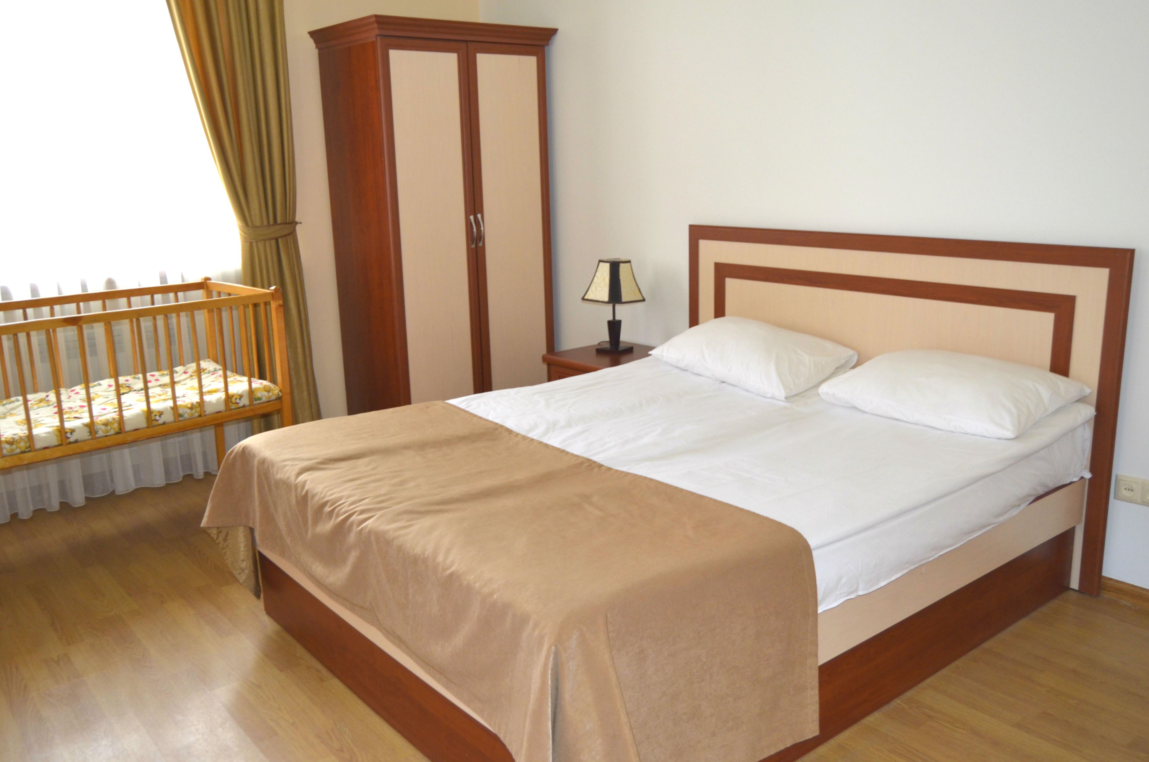 Un dormitorio con cama de madera, mesita de noche con lámpara, armario y cuna.