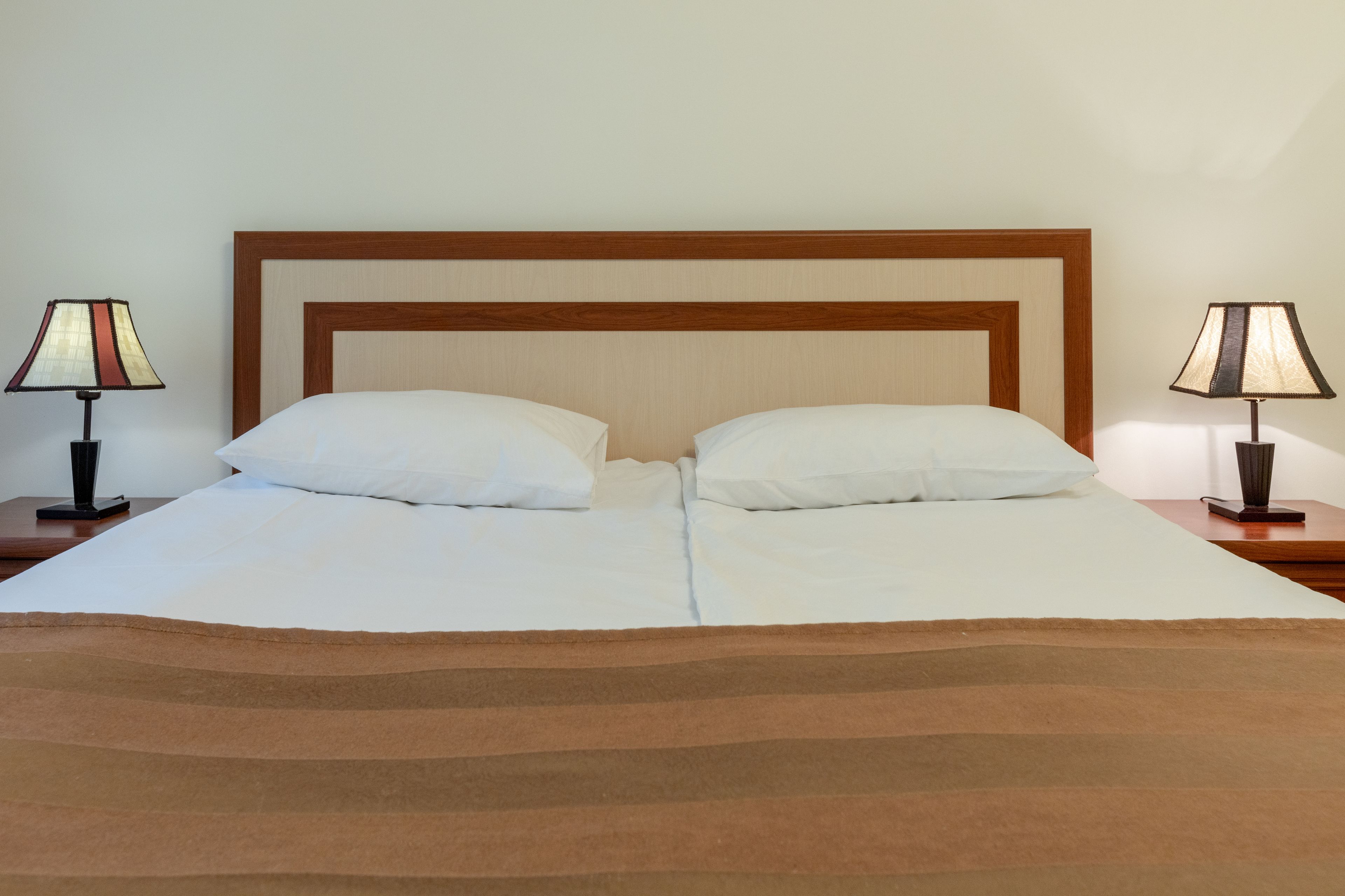 Una cama doble con cabecera de madera, dos mesitas de noche con lámparas y un edredón marrón a rayas.