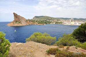 Ett kustlandskap med en markant klippformation, en stad i bakgrunden och havet.