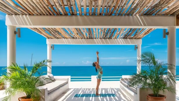 A covered outdoor area with a view of the sea, featuring a person performing a yoga pose. - Four Bedroom Ecoluxe Haven in Treasure Beach with Pool (Treasure Beach)