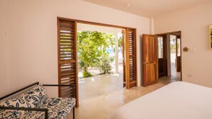 A bedroom with a bed, a bedside table, and a view of a beach through open doors. - Four Bedroom Ecoluxe Haven in Treasure Beach with Pool (Treasure Beach)