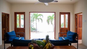A room with two blue sofas, a wooden table with a fruit bowl, and a ceiling fan. - Four Bedroom Ecoluxe Haven in Treasure Beach with Pool (Treasure Beach)