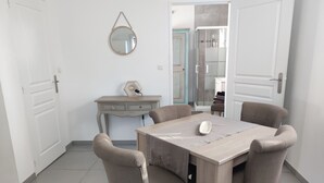 A dining area with a wooden table, four chairs, a small desk with drawers, a hanging mirror, and a door leading to a shower area. - 2-room villa with a terrace and a view of the pool. (Fréus)
