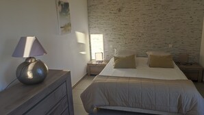 A bedroom with a bed, a nightstand, a lamp, a dresser, and a brick-patterned wall. - 2-room villa with a terrace and a view of the pool. (Fréus)