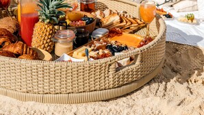 Ein Picknick am Strand mit einem Korb voller Essen und Getränke, einer Ananas und Blick aufs Meer.