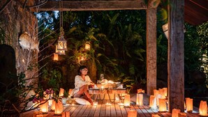 Eine Holzterrasse mit gedecktem Tisch, umgeben von Papierlampen, in tropischer Umgebung.