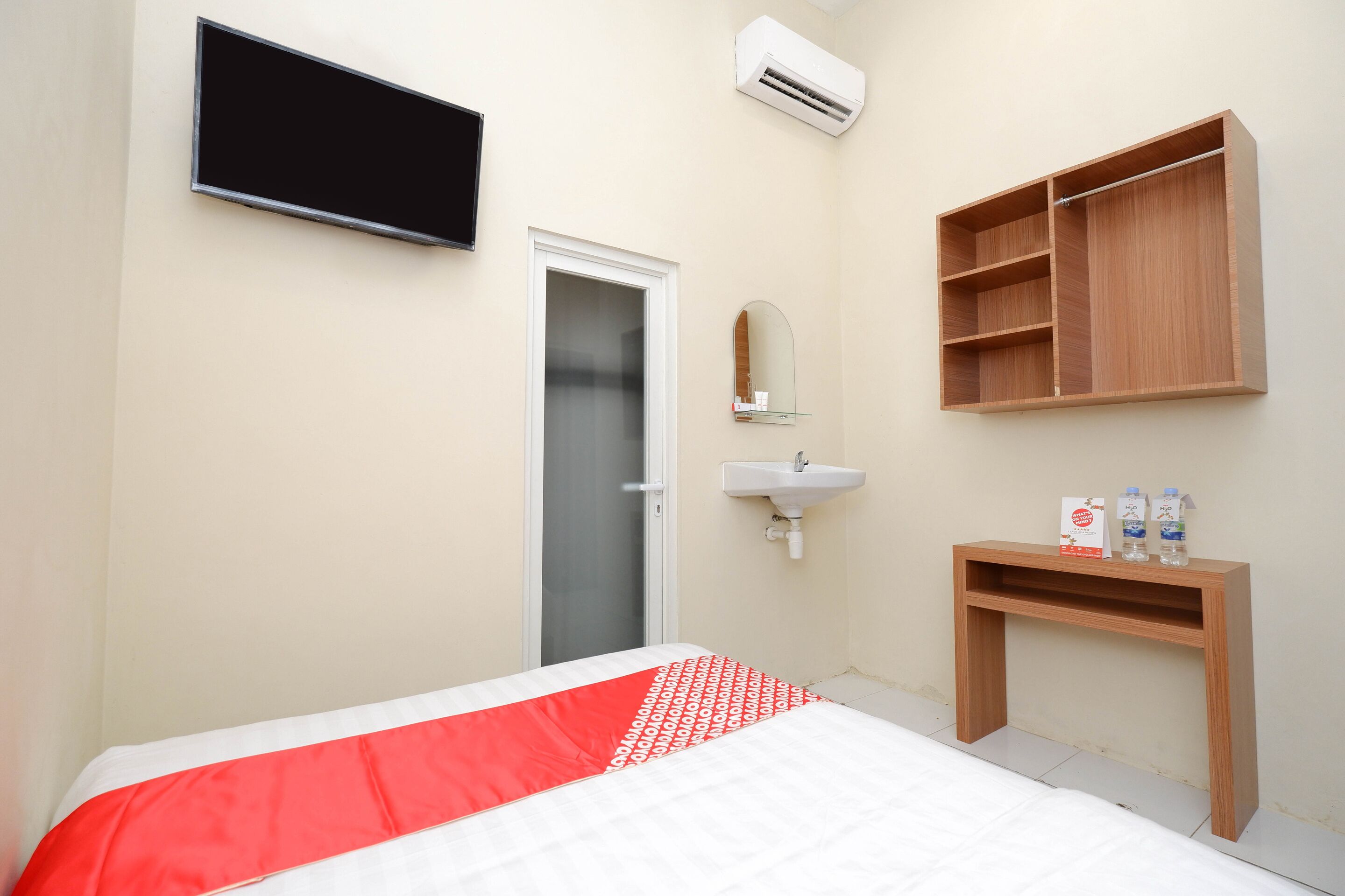 A bedroom with a bed, a bedside table, a mirror, a wardrobe, and a TV mounted on the wall.
