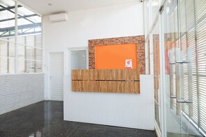 A reception desk with a wooden panel and an orange board, a glass door, and a white brick wall. - Hotel O Unta Residence (Semarang)