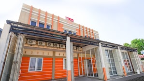Ein Gebäude mit roter und beiger Fassade, großen Fenstern und einem überdachten Eingangsbereich.