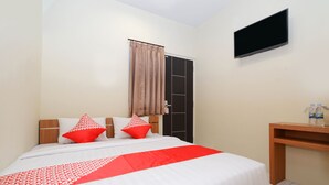 Ein Hotelzimmer mit Bett, Wandfernseher, Schreibtisch und einer Tür.