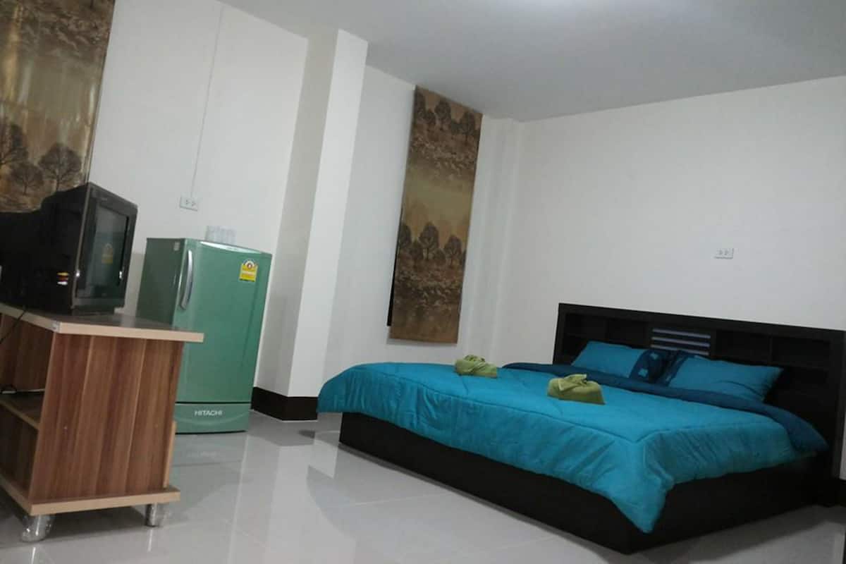 A bedroom with a bed, a desk with a computer, a refrigerator, and a wall-mounted TV.