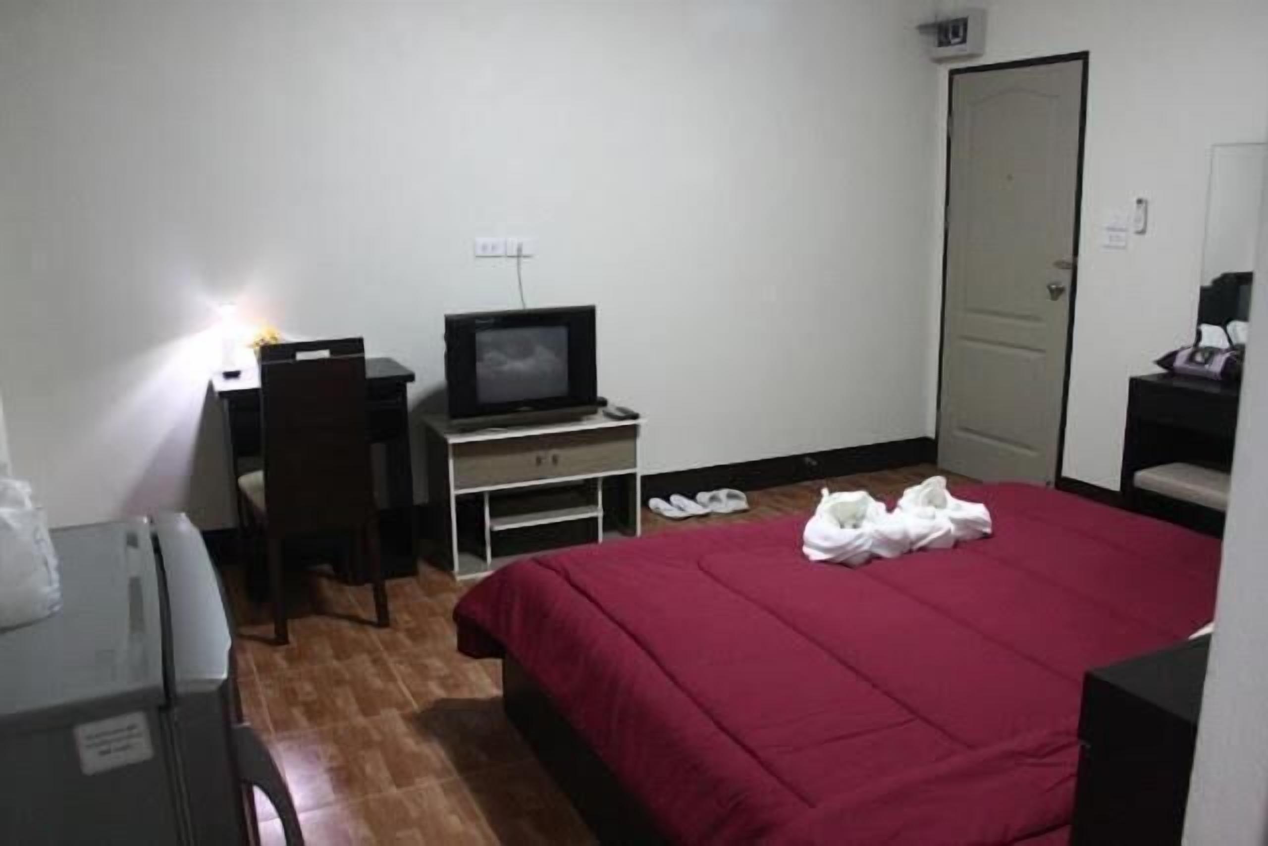 A hotel room with a bed, a desk with a computer, a chair, and a TV.