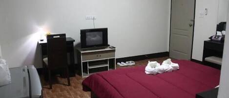 A hotel room with a bed, a desk with a computer, a chair, and a TV.