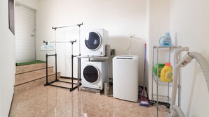 Una sala de bugaderia amb rentadora, assecadora i taula de planxa.