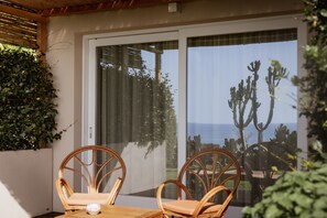 Un coin repas avec des chaises en osier et une table en bois, donnant sur un jardin planté de cactus et offrant une vue sur l’océan.