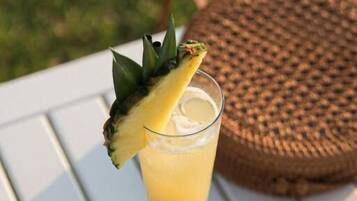 Un bicchiere di una bevanda gialla con una fetta di ananas, occhiali da sole e un menu su un tavolo bianco.