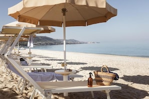 A beachside lounge area with sun loungers, a table, and a beach umbrella. - Armacera Resort (Zambrone)