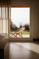 Una habitación con cama, ventana que da a un jardín y una silla de madera afuera.