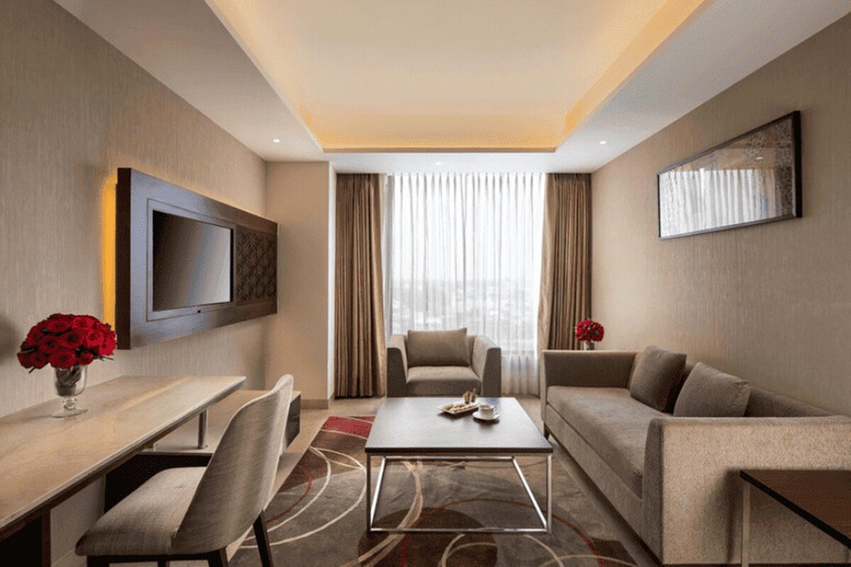 Une chambre d’hôtel moderne équipée d’un téléviseur à écran plat, d’un canapé, d’une table basse et d’un coin repas.