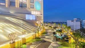 Una terraza en la azotea con mobiliario exterior, plantas en macetas y vistas de la ciudad.