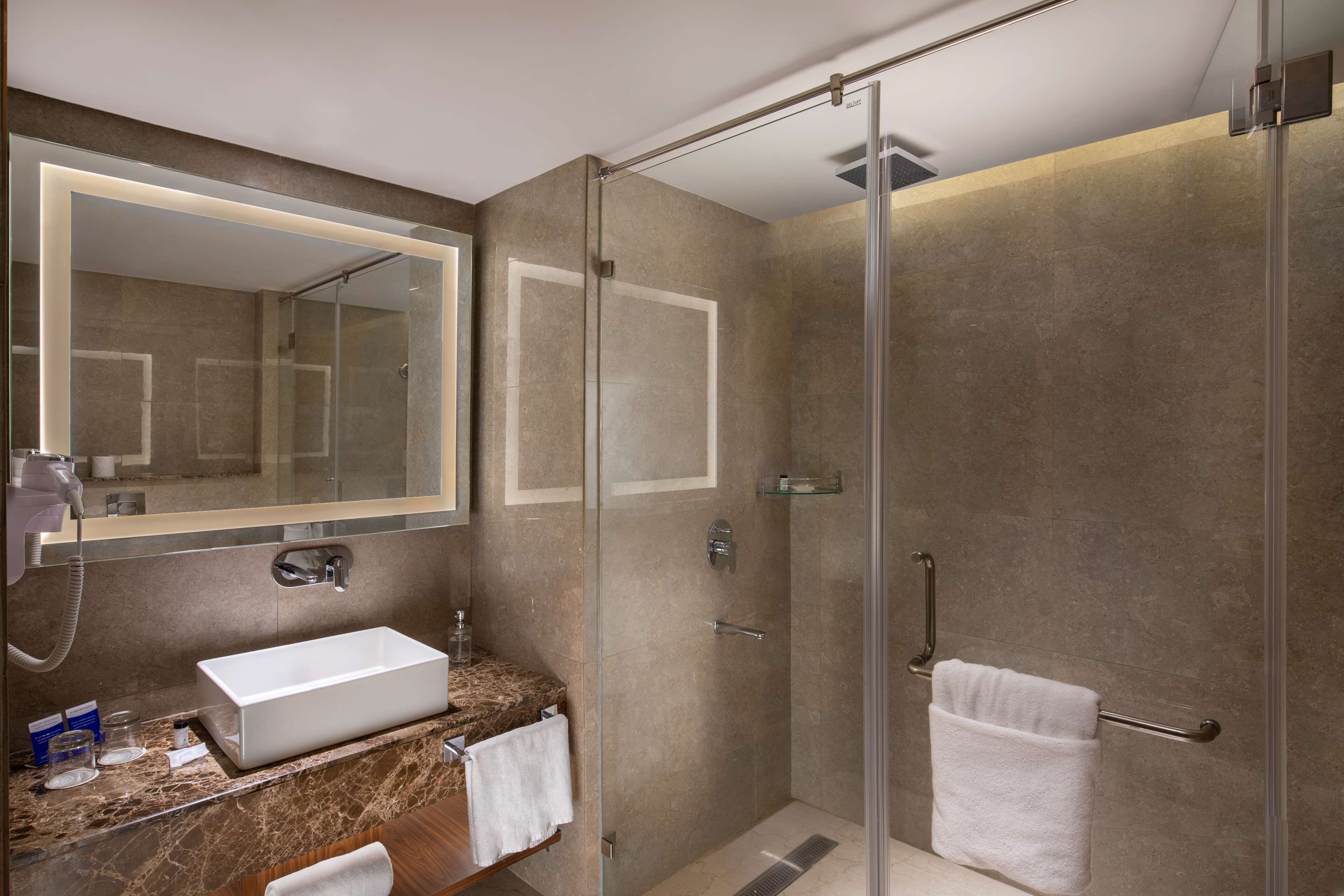 Un baño moderno con ducha de vidrio, lavabo blanco y espejo grande.