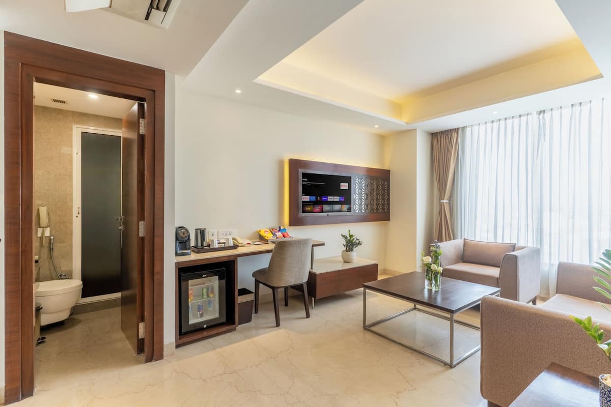 A hotel room with a desk, chair, sofa, coffee table, and a TV mounted on the wall.