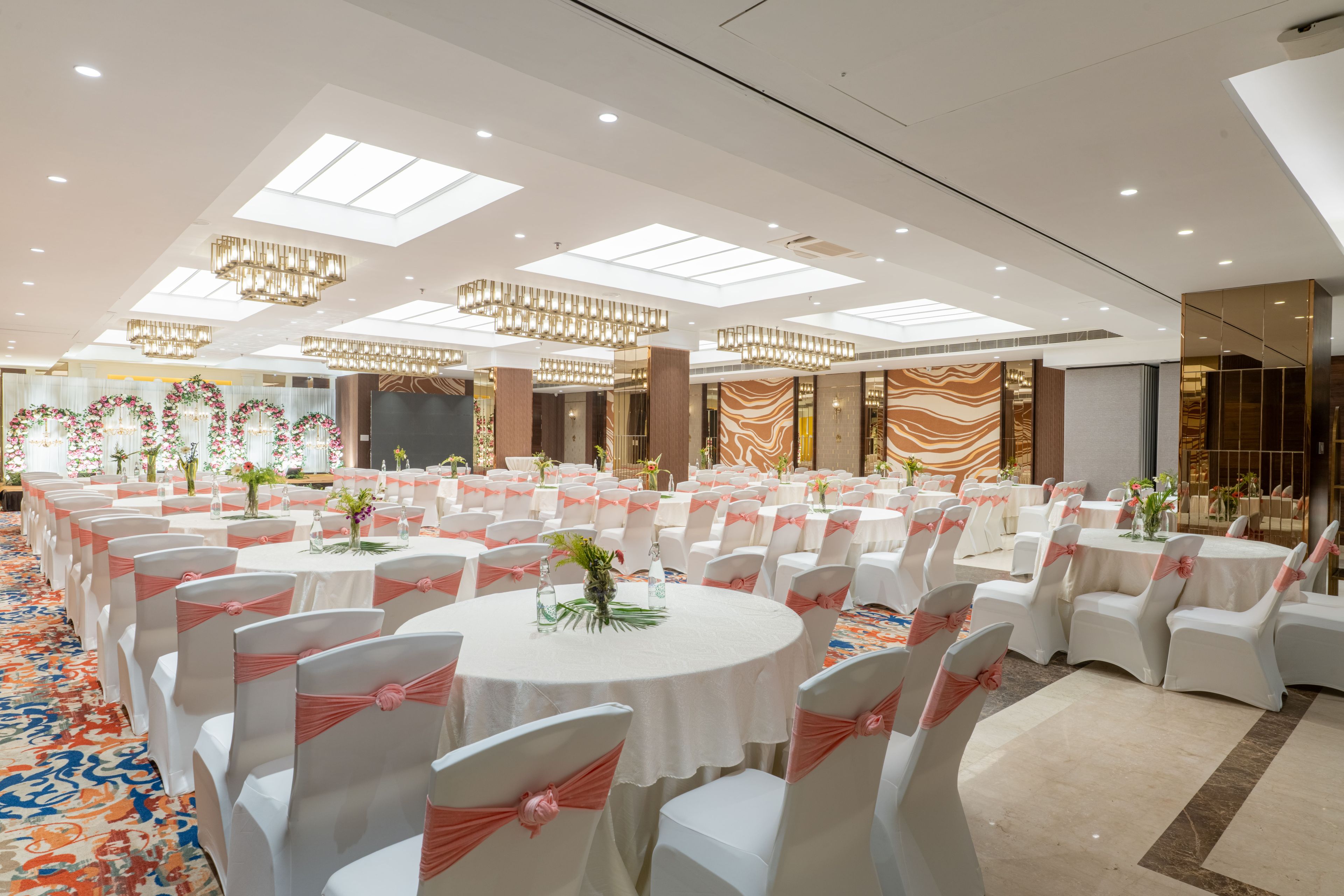 Een balzaal met ronde tafels, witte stoelen en roze linten.
