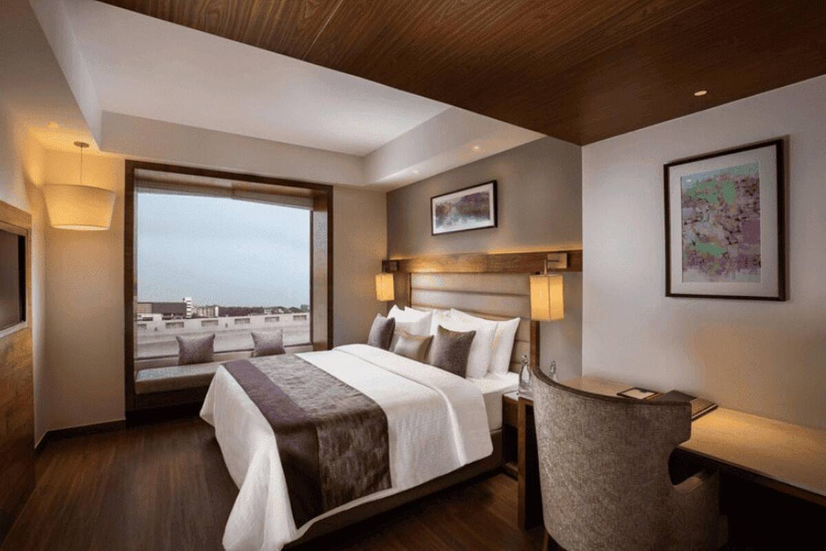 A hotel room with a large bed, bedside lamps, a desk, and a window with a city view.