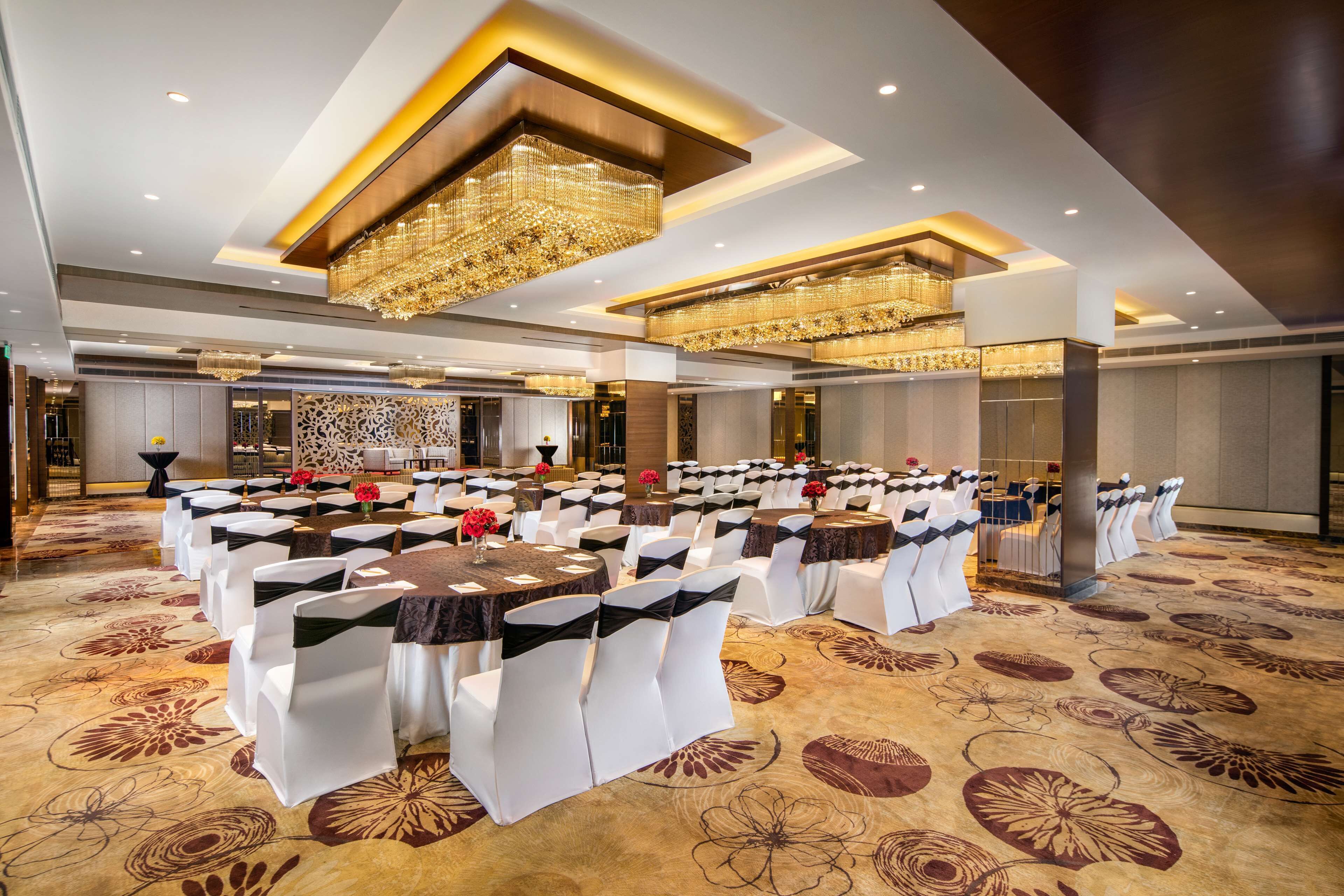 A banquet hall with rows of tables and chairs, chandeliers, and a patterned carpet.
