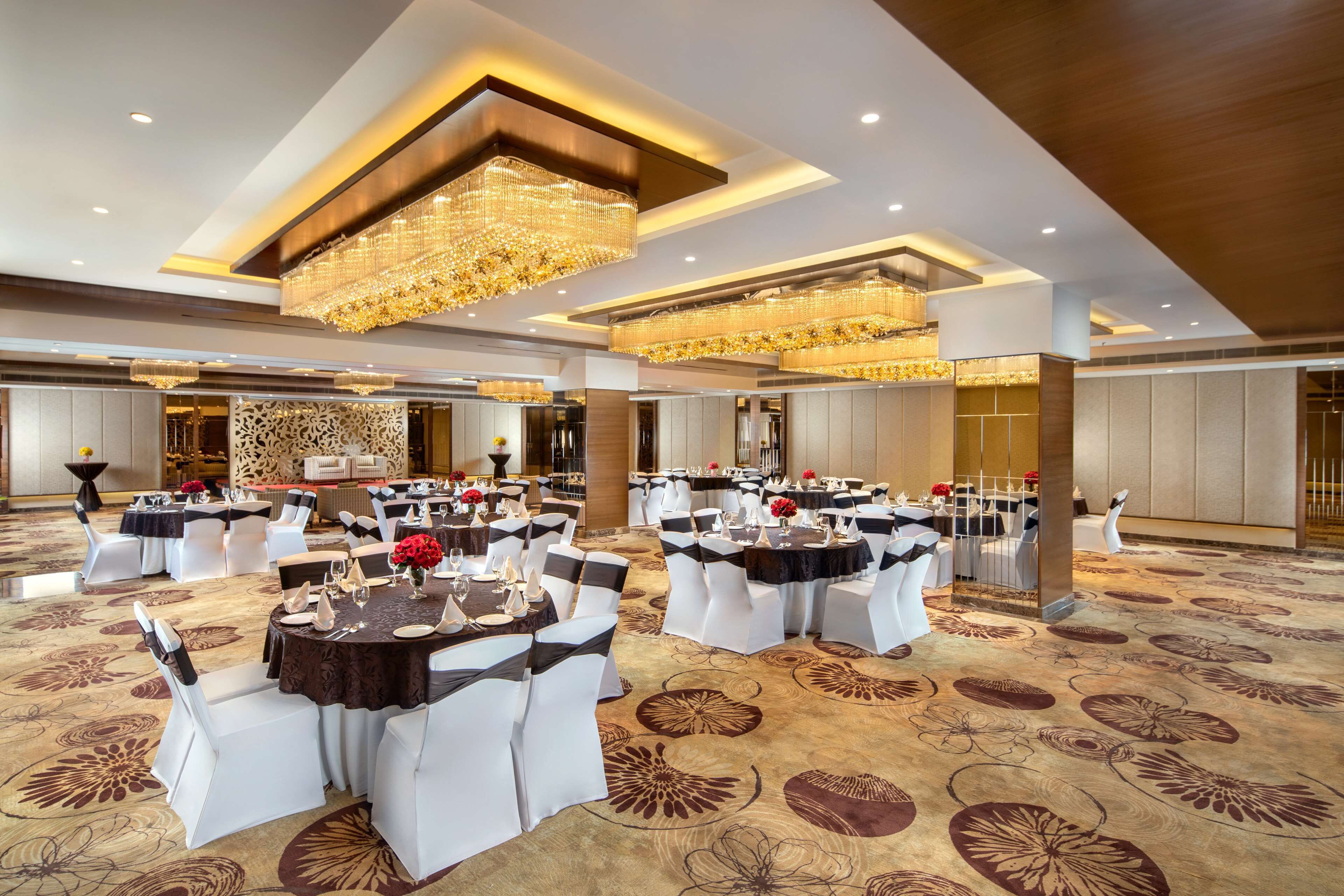 A banquet hall with round tables, white chairs, and chandeliers.